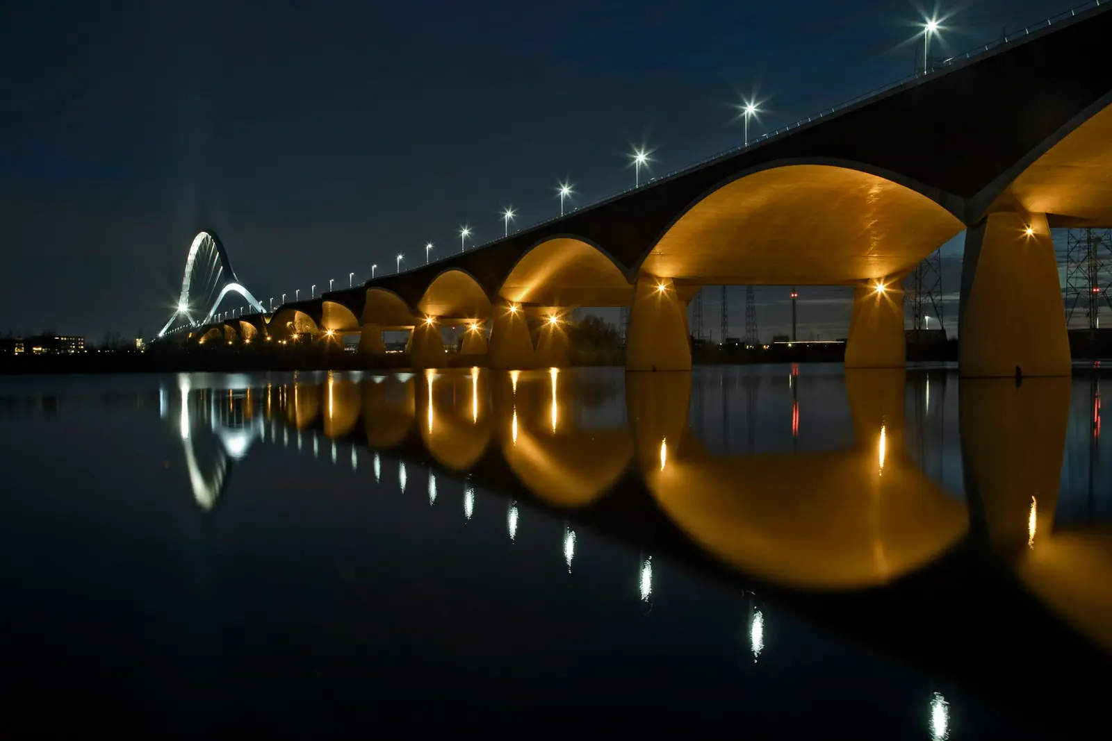 Brug De Oversteek over de Waal bij Nijmegen bij nacht, met verlichte bogen gespiegeld in het water