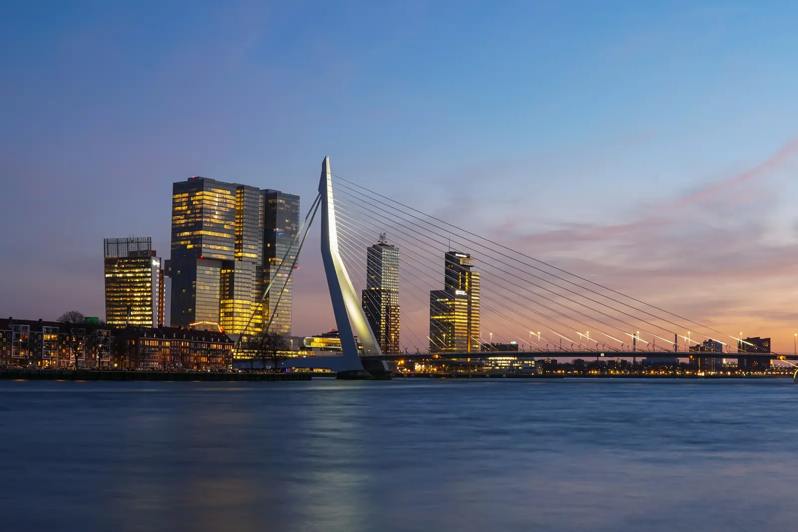 Erasmusbrug en de skyline van de Kop van Zuid in Rotterdam in de avondschemering, gespiegeld in de Maas
