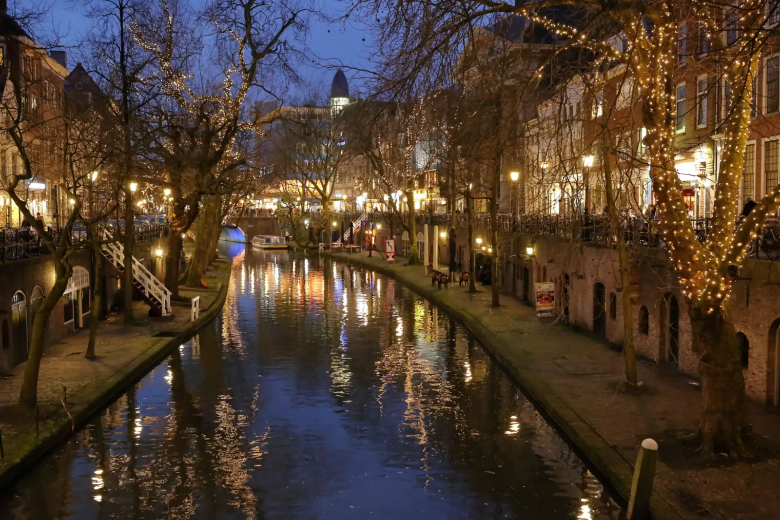 Oudegracht in Utrecht bij avond, met lichtjes in de bomen weerspiegeld in het water
