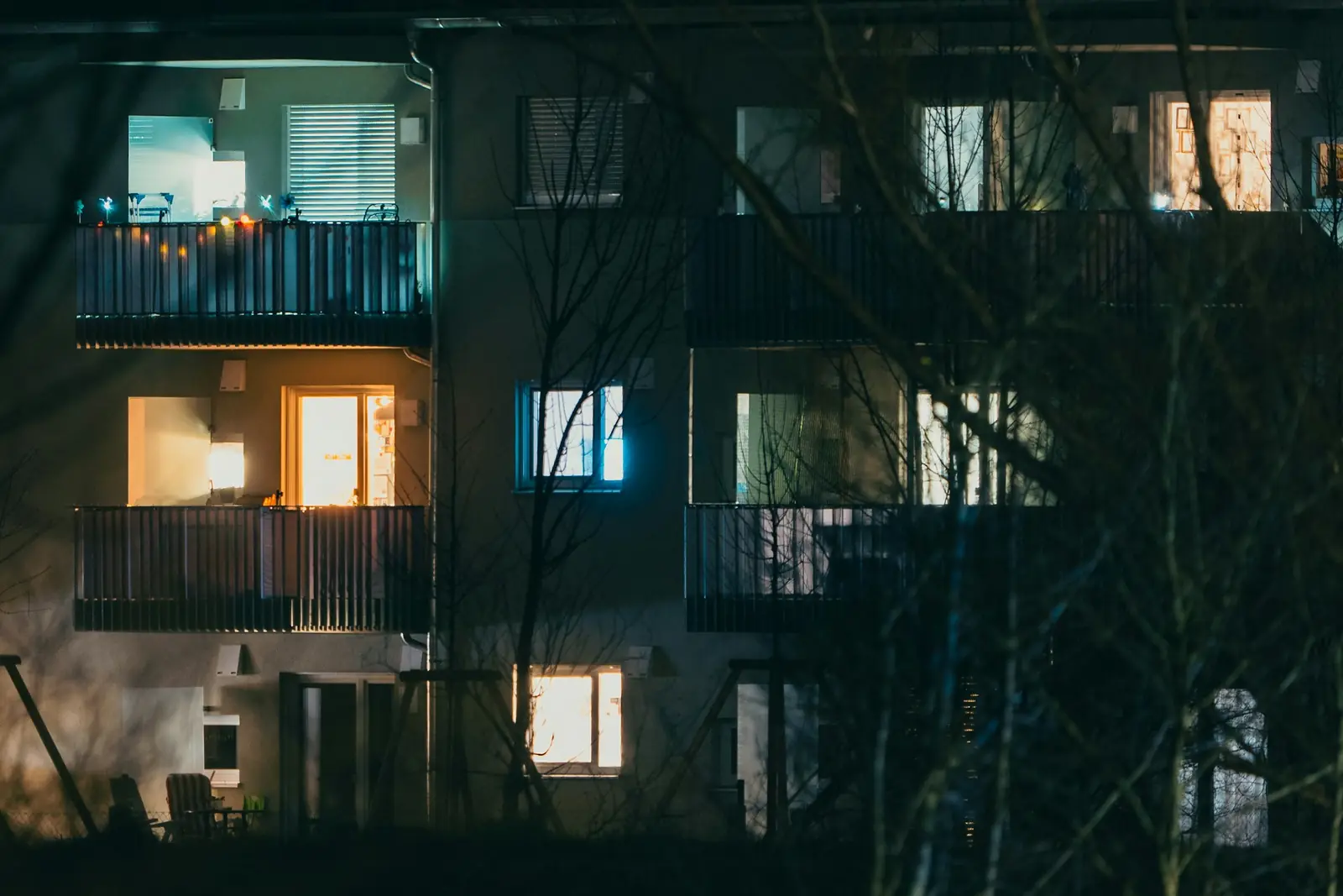 Woongebouw bij avond met balkons en enkele verlichte ramen achter kale takken