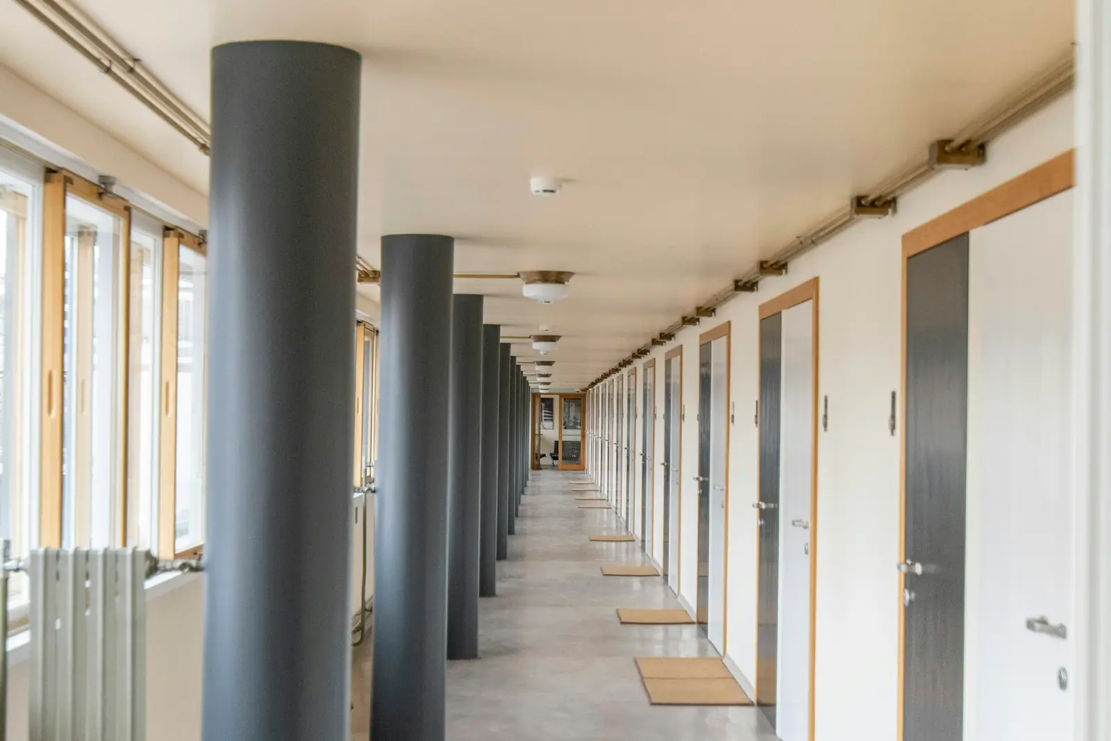 Lichte, lange gang in een zorggebouw met deuren aan één kant en ramen en zuilen aan de andere